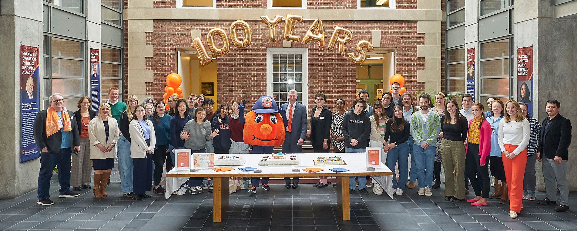 Photo of Maxwell faculty and staff celebrating 100 years of Maxwell with cake and Otto