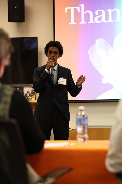 Person speaking at a microphone in front of a screen displaying the word