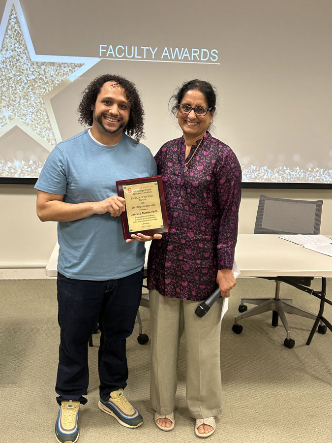 Two individuals stand together with an award between them