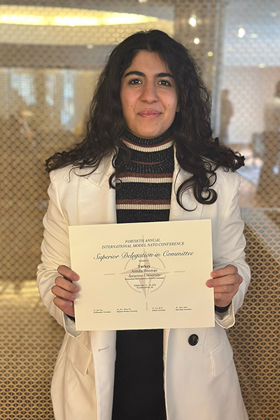 Individual holding a certificate from the International Model United Nations Conference on the Syrian Refugee Committee, smiling in an indoor setting.