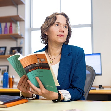 Person sitting at a desk in an office, holding a book titled "SNAP Matters," looking contemplative.