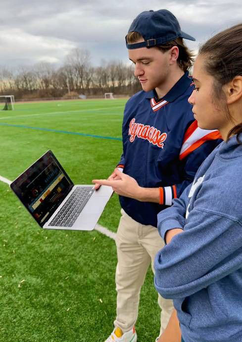 Dan Griffith on field show stats on computer to another student