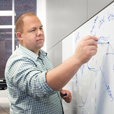 Person writing on a whiteboard with a marker in a classroom or office setting.