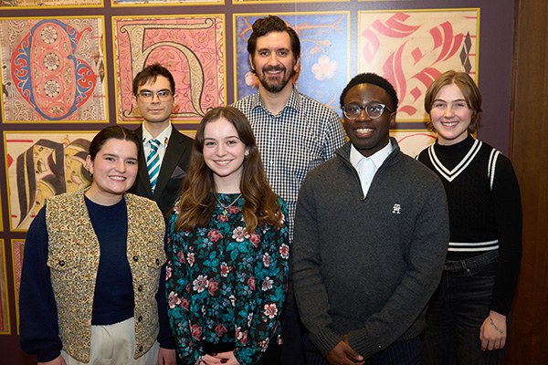 Group of six individuals smiling in front of a colorful, patterned wall with artistic designs.