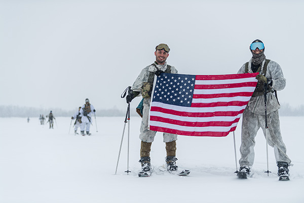 Two individuals in winter gear holding an American flag, standing in a snowy landscape.