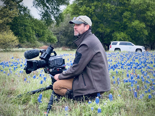 Photo of Jack Herrle holding a video camera in a field of wildflowers