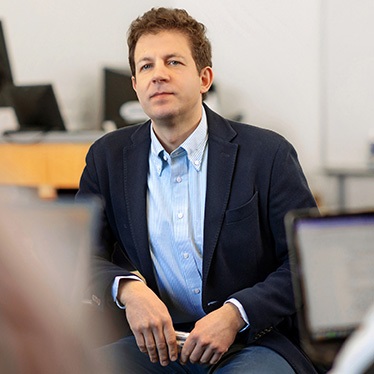 Person in business attire sitting in an office environment and looking attentively to the side.