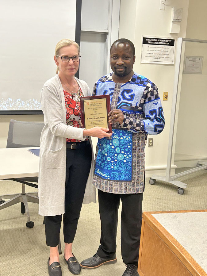 Two individuals stand together with an award between them