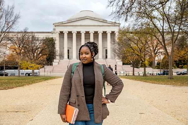 Person standing in front of the National Gallery of Art in Washington D.C., holding a book and wearing a plaid blazer.