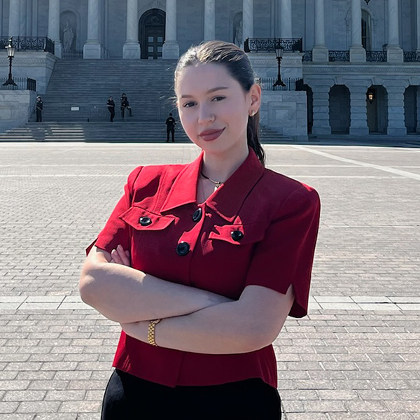 Individual in a red blouse standing confidently in front of the United States Capitol building.