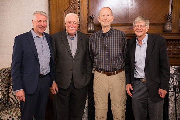 Four individuals, standing side by side, smiling, in a room with elegant vintage decor.