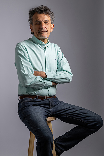 Portrait of an individual standing with arms crossed, wearing a light green shirt with a small Lacoste logo, against a gray backdrop.