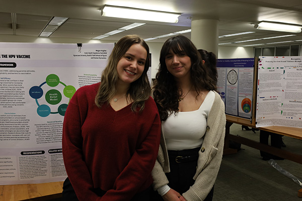Two individuals smiling, standing in front of a poster titled
