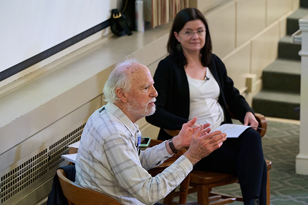 Robert Shetterly, seated and gesturing during a discussion, with an attentive audience member next to him.