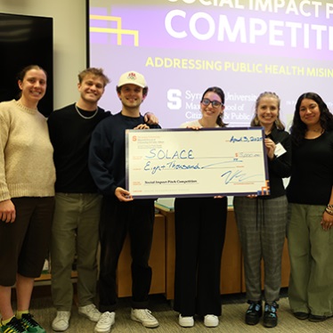 Group of five individuals posing with an oversized check from Syracuse University, awarded to "Solace" for $5,000 at a social impact competition.
