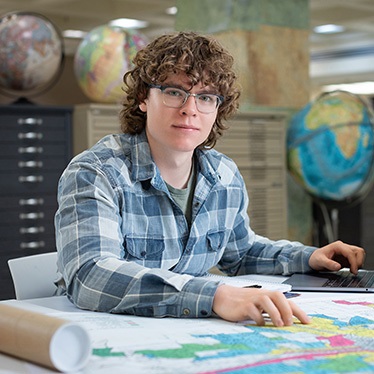 Person using a computer in a library filled with globes and maps.