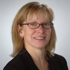 Portrait of a smiling individual with glasses, wearing a dark blazer.