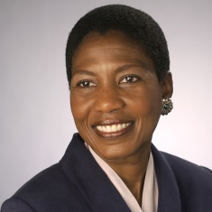 Portrait of a smiling individual wearing a dark blazer and silver earrings.