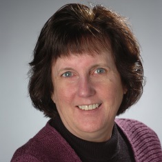 Portrait of a smiling person with short brown hair wearing a purple sweater.