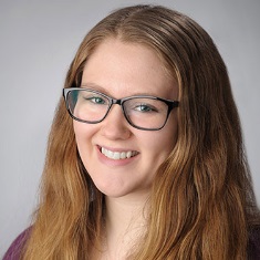 Portrait of a smiling person with glasses, wearing a purple sweater.