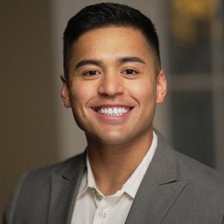 Portrait of a person smiling, wearing a gray suit jacket and a light shirt.