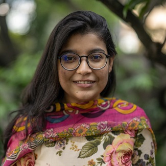 Photo of a young woman with dark hair, glasses and a colorful top.