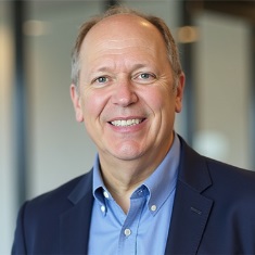 Person smiling in a professional setting, wearing a blue blazer and light blue shirt.