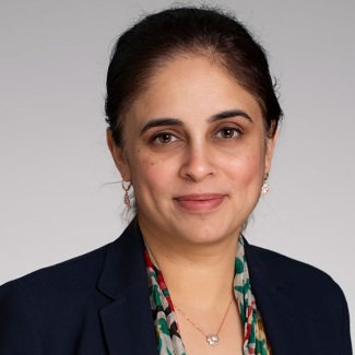 Portrait of an individual wearing a dark blazer and a patterned scarf, with a subtle smile.