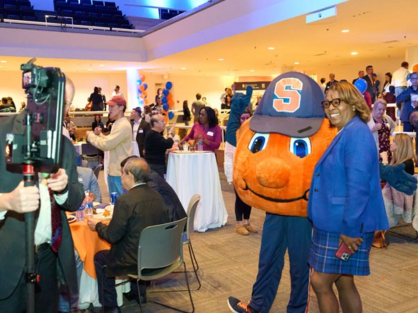 Otto takes a photo with an event attendee. Attendees in the background are enjoying food, drinks, and good company.
